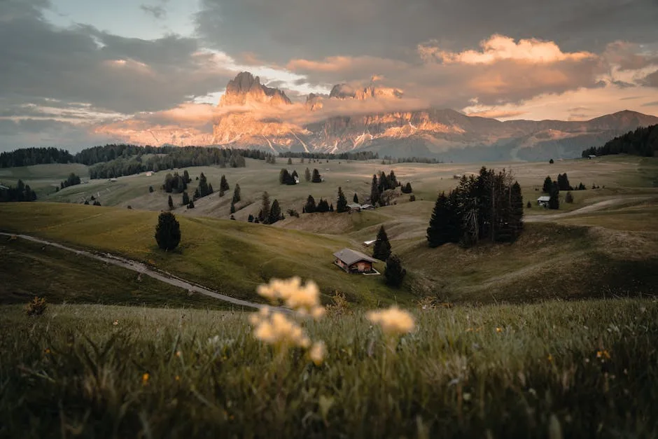 Prairie ondulante et chalets devant sommets des Dolomites au coucher de soleil