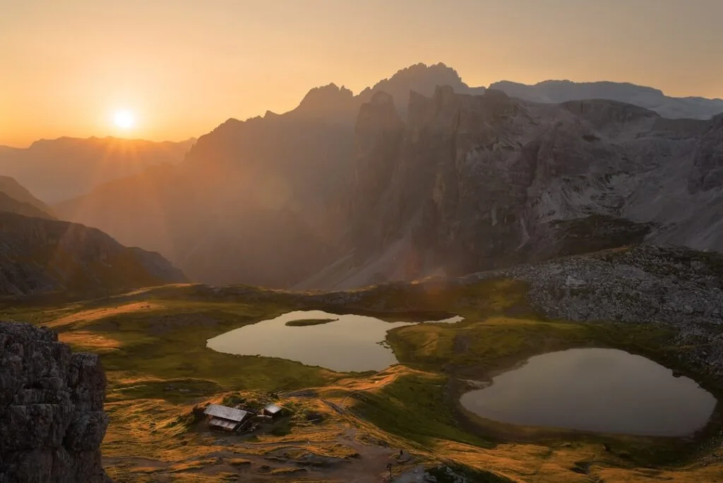 Lacs alpins reflétant le soleil couchant, chalets et sommets des Dolomites