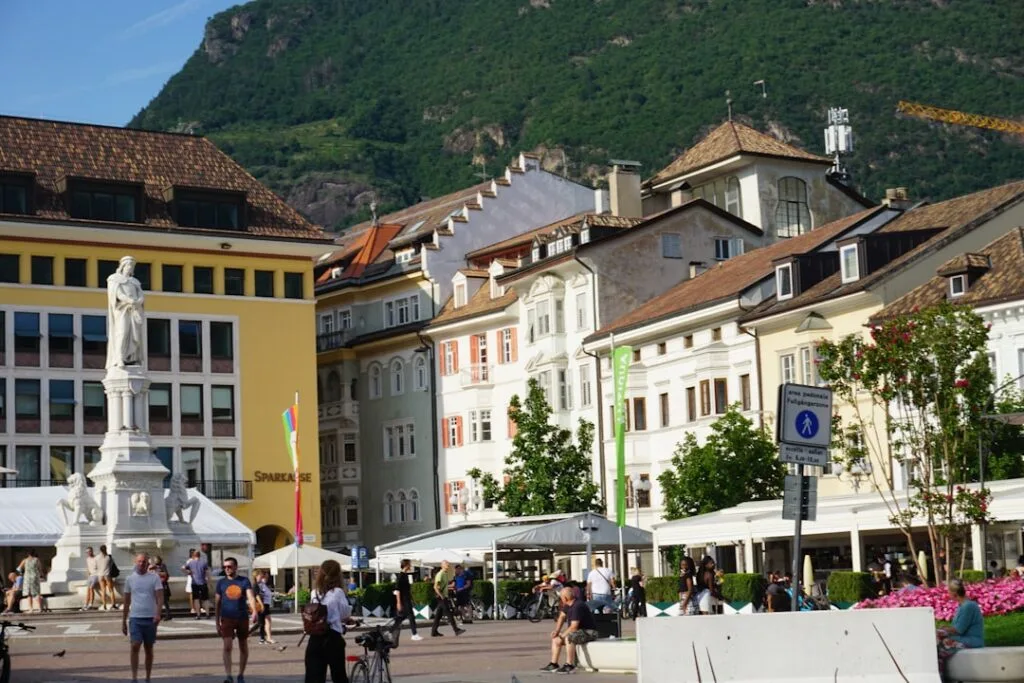Place animée avec une statue et façades colorées au pied des Dolomites