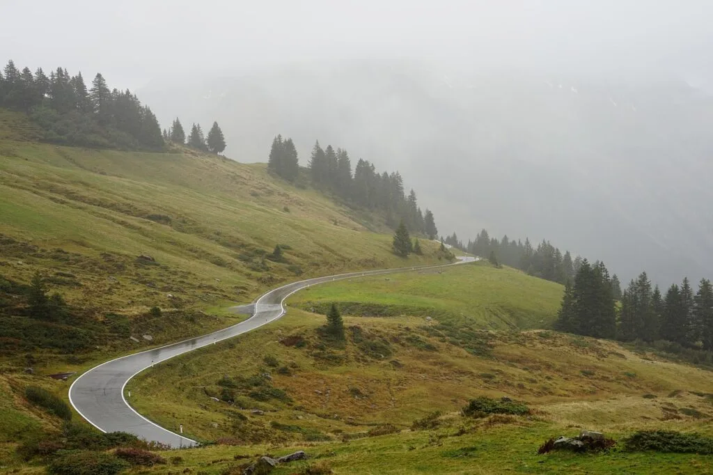 Route sinueuse mouillée traversant alpage brumeux des Dolomites