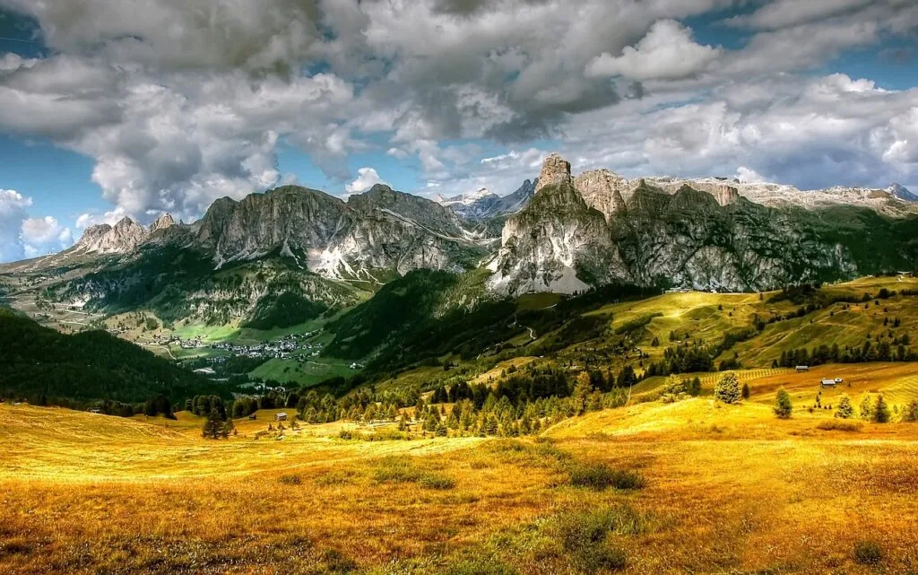 Prairie dorée et vallée avec village, falaises monumentales des Dolomites