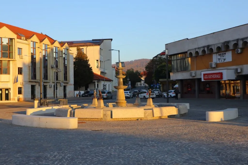 Place pavée avec fontaine centrale et commerces au fond ensoleillés