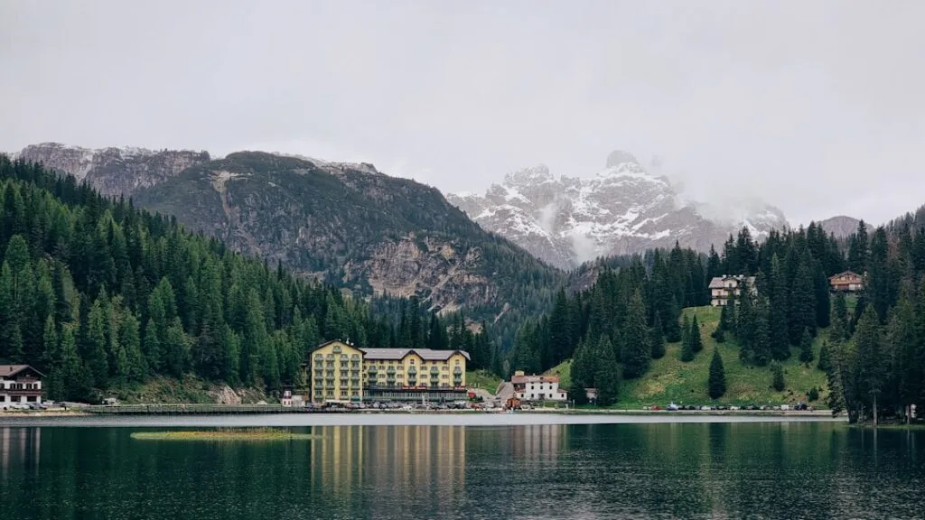 Hôtel jaune au bord du lac entouré de sapins dans les Dolomites