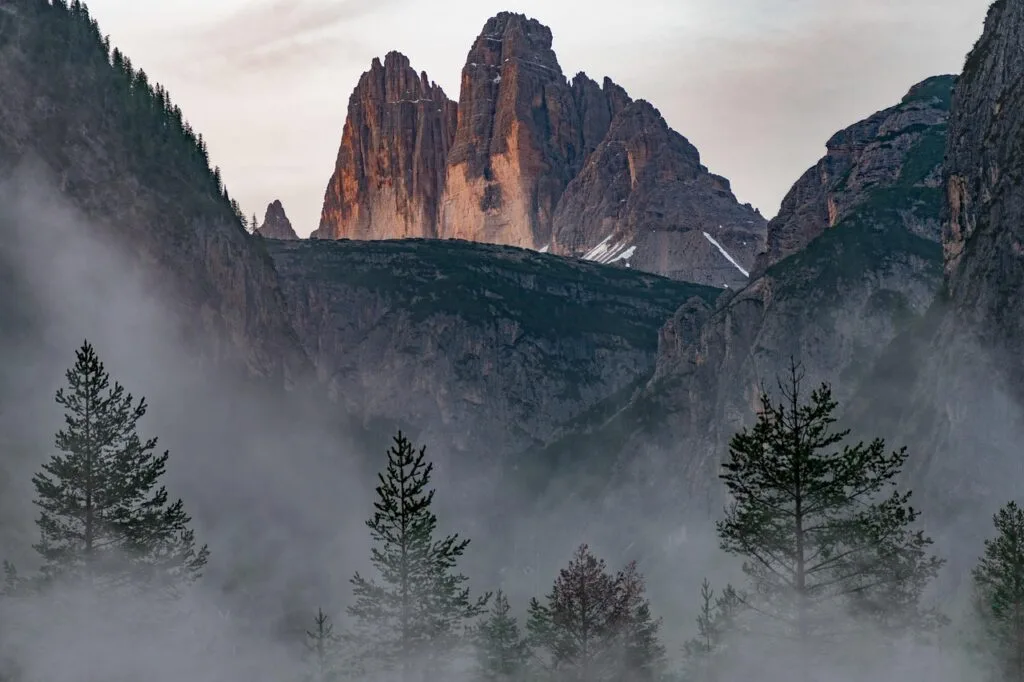 Pics rocheux des Dolomites illuminés, sapins noyés dans la brume