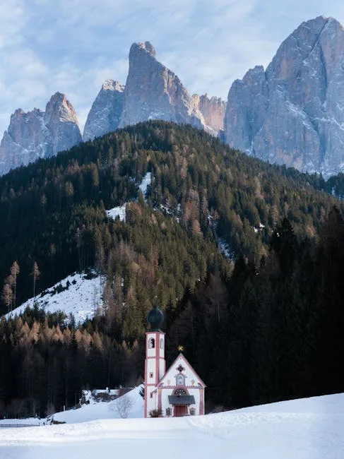 Église baroque au premier plan, sapins et sommets des Dolomites