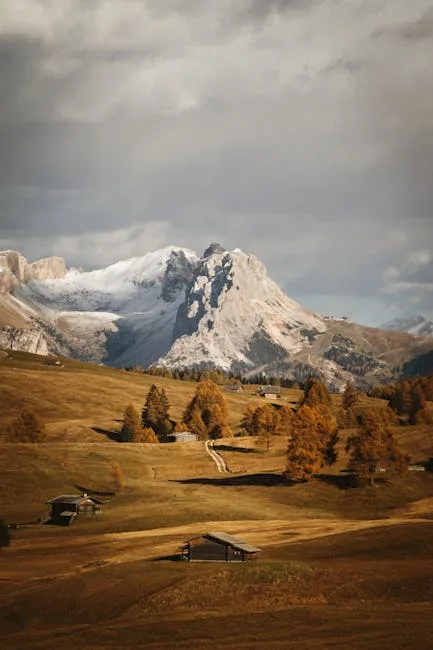 Prairie d'alpage avec chalets et montagne enneigée aux Dolomites