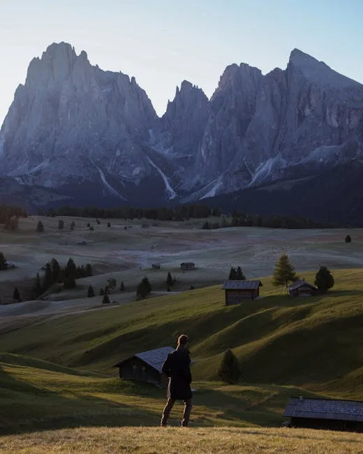 Randonneur observe prairies vallonnées et sommets abrupts des Dolomites au crépuscule