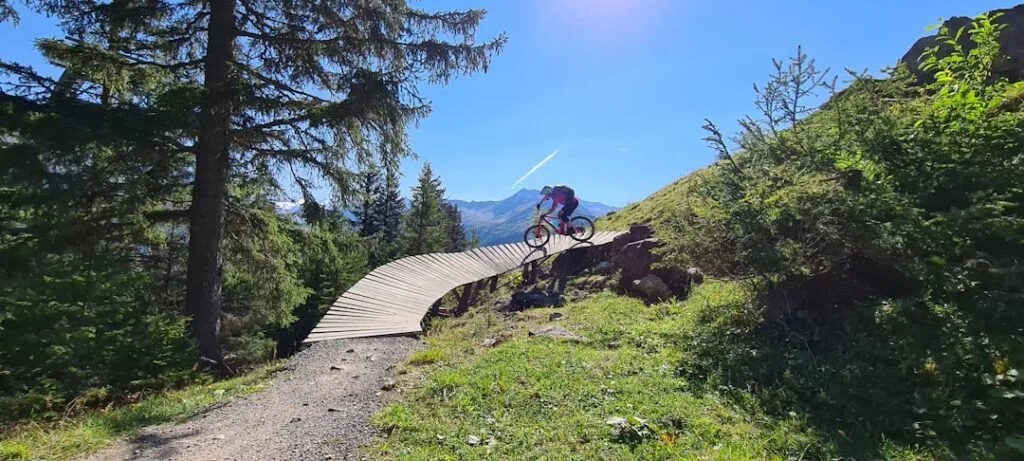 VTTiste franchissant une passerelle en bois sur un sentier ensoleillé des Dolomites