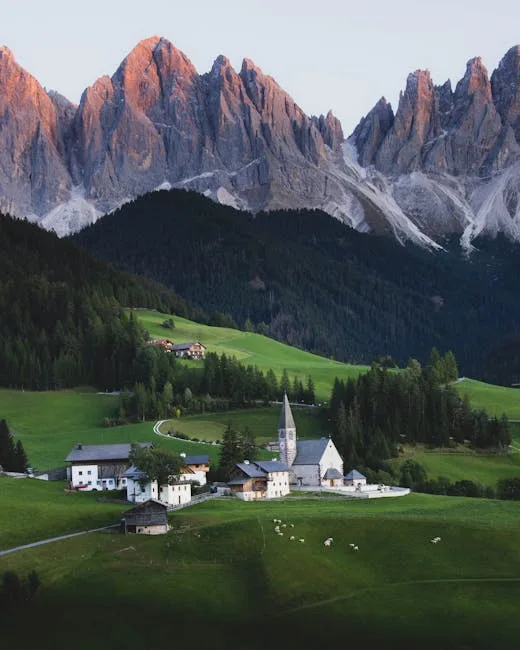 Village alpin avec clocher et prés, massifs escarpés des Dolomites