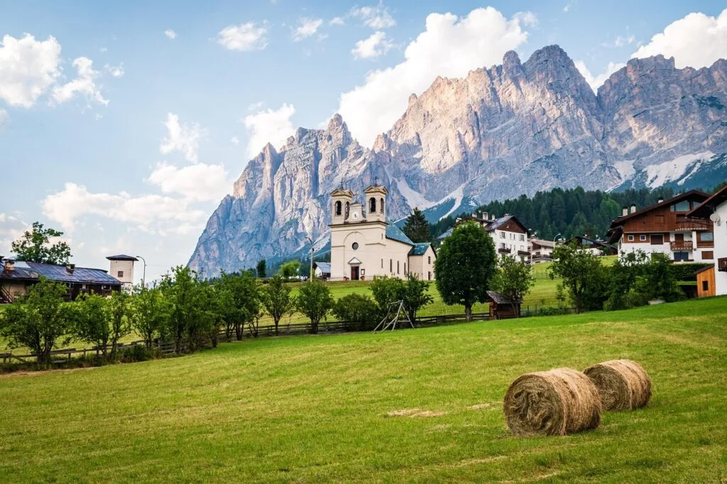 Village alpin et meules de foin devant les parois des Dolomites