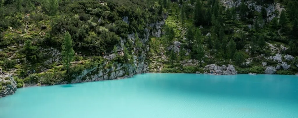 Eau turquoise d'un lac alpin encadrée de rochers et de sapins dans les Dolomites