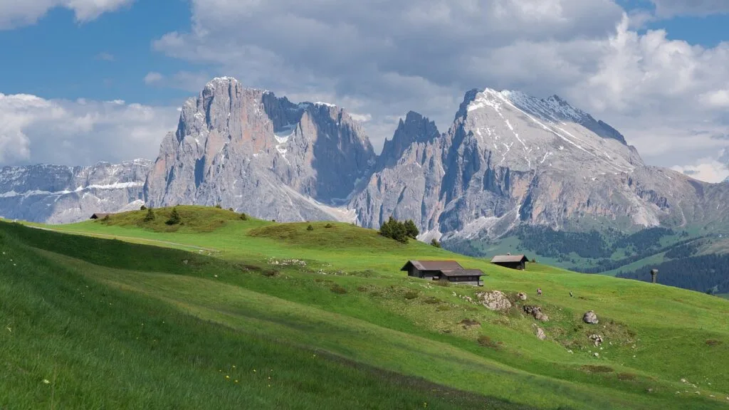 Chalets isolés sur alpage vert avec montagnes des Dolomites en arrière-plan