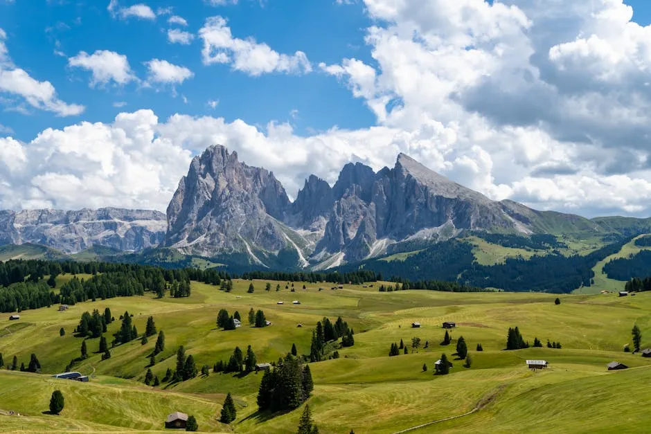 Prairie verte parsemée de chalets devant les Dolomites imposantes