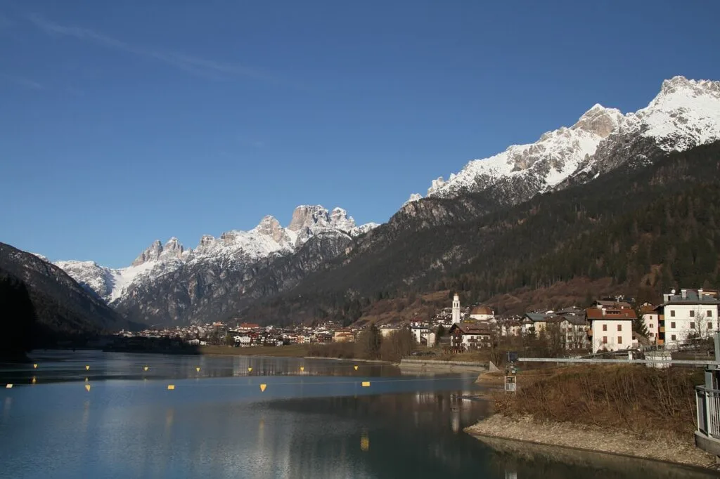 Village alpin au bord d’un lac, montagnes enneigées des Dolomites