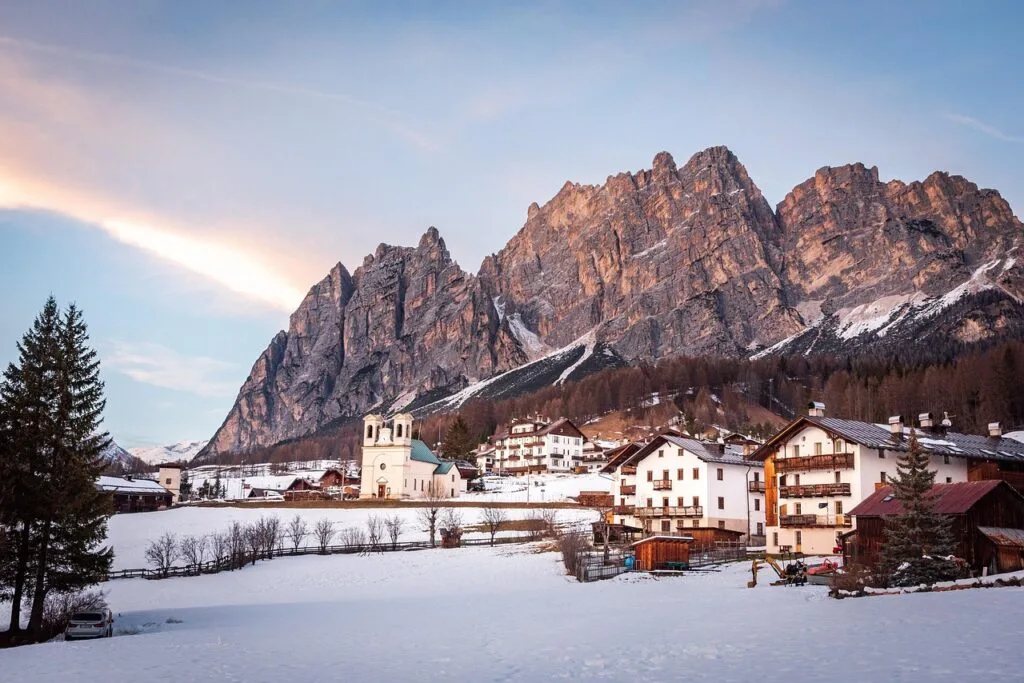 Village enneigé au pied des sommets rocheux des Dolomites