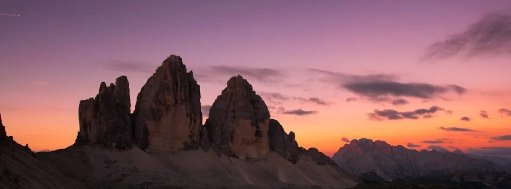 Trois aiguilles rocheuses des Dolomites silhouettées au coucher de soleil violet